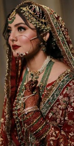 a woman in a red and gold bridal outfit with jewelry on her head,