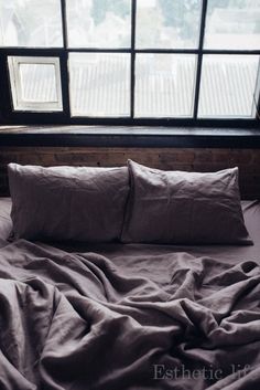 an unmade bed with two pillows in front of a window