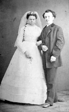 an old black and white photo of a man and woman in wedding attire standing next to each other