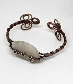 This is a beautiful handmade piece created by Mimi.  This cuff bracelet was made with antique copper 14 gauge and 22 gauge  copper wire.  The stone is an unpolished white beach quartz from Topsail Island NC and is accentuated by two copper swirls. The bracelet is adjustable   About this stone: Some of the NC's beaches have rock pebbles. These Pebbles are derived from older sediment now being reworked in the near shore environment or from offshore rock out-crops on the sea floor. One interesting pebble type consist entirely of quartz that once existed in veins or bands in the original rock....Geologist believe that this gravel like the pebbles are derived from old river beds that once traversed the continental shelf when sea level was lower during ice ages. These deposits now lie beneath th Handmade Bohemian Copper Wire Cuff Bracelet, Bohemian Copper Wire Cuff Bangle Bracelet, Adjustable Wire Wrapped Bronze Cuff Bracelet, Handmade Copper Wire Cuff Bangle, Handmade Copper Wire Cuff Bracelet Bangle, Bohemian Copper Wire Bangle Bracelet, Bohemian Bangle Bracelet In Copper Wire, Bohemian Copper Wire Wrapped Cuff Bracelet, Unique Copper Wire Wrapped Cuff Bracelet