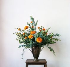 an arrangement of flowers in a vase on a stool against a white wall with wood flooring