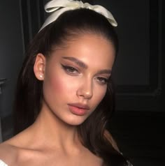 a woman with long dark hair wearing a white top and bow in her hair is looking at the camera