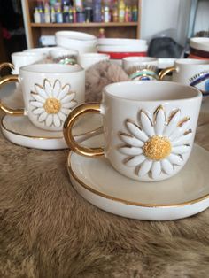 four coffee cups and saucers with gold rims on a fur covered table top