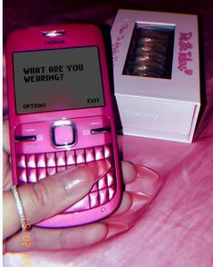 a pink cell phone sitting on top of a bed next to a box with the message what are you wearing?