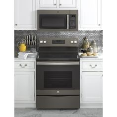 an oven and microwave in a kitchen with white cabinets on the counter top, along with utensils