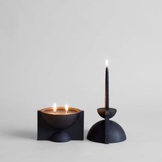 two candles sitting next to each other on top of a black stand with one candle lit