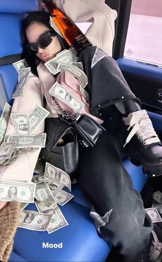 a man in sunglasses and black pants sitting on a blue car seat with money all over his legs