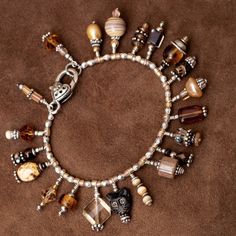 a bracelet with many charms on it sitting on a brown carpeted floor next to a bottle of wine