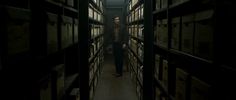 a man standing in the middle of a long dark room filled with shelves full of files