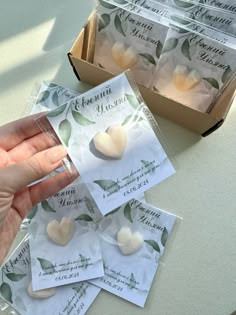 a person is holding some white heart shaped candies in front of a box with green leaves on it