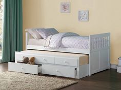 a white bed with drawers underneath it in a room next to a rug and window