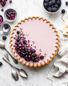 a pie topped with berries and blackberries sitting on top of a table next to silverware