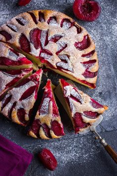 a cake with slices cut out and covered in powdered sugar on a table next to cherries