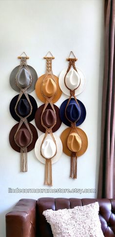 a brown leather couch sitting next to a wall hanging with hats and tassels