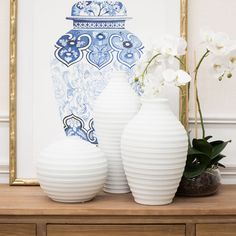 two white vases sitting next to each other on a wooden table in front of a blue and white wall