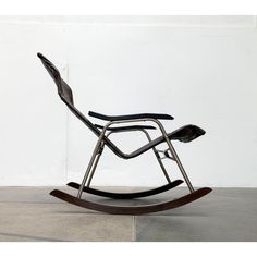 a metal rocking chair sitting on top of a cement floor next to a white wall