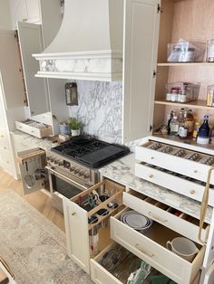 an open drawer in the middle of a kitchen with white cabinets and marble counter tops