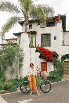 a woman standing next to a bike in front of a house