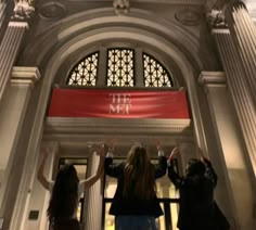 three women are standing in front of the met building with their hands up and arms raised