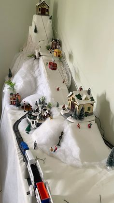 a toy train set up in the middle of a snow - covered hill with houses and trees