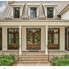 a white house with two brown doors and steps leading up to the front door is surrounded by greenery