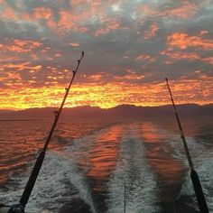 two fishing rods on the back of a boat in the ocean at sunset with mountains in the background