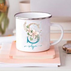 a white coffee mug sitting on top of a wooden coaster next to a pink flower