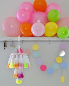 balloons and tassels are hanging on the wall in front of a white shelf