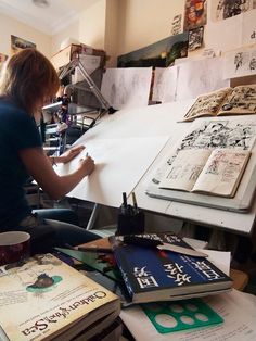 a woman sitting at a table with lots of books and papers on top of it