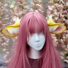 a wig with pink hair and yellow horns on it's head, sitting in front of flowers