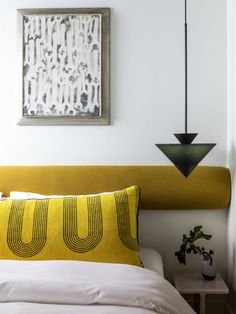 a bed with a yellow headboard next to a painting on the wall above it