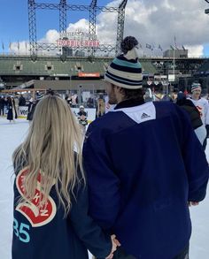 a man and woman standing on top of an ice rink holding hands while looking at the scoreboard