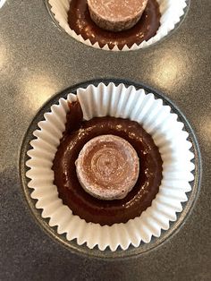 two cupcakes with chocolate frosting sitting in paper cups on a counter top