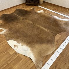 a brown and white cowhide rug on a wooden floor with measuring tape around it