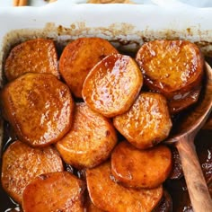 cooked sweet potatoes in a casserole dish with brown sauce and wooden spoons