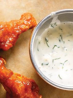 a metal bowl filled with sauce next to chicken wings