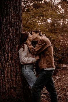 a man and woman kissing in front of a tree with leaves on the ground around them