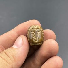 a hand holding a small gold object in it's left hand, with the head of a buddha