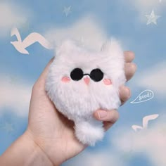 a hand holding a small white stuffed animal with black glasses on it's eyes