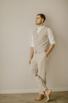 a man standing in front of a white wall with his hands on his hips wearing a vest and pants