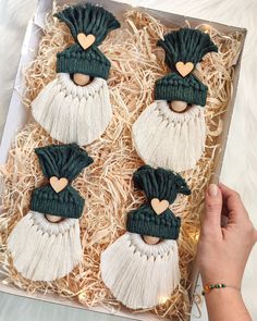 four decorated cookies with tassels and hearts in a box on top of straw