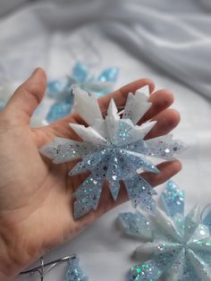 a hand is holding some snowflakes on a white sheet with blue sequins