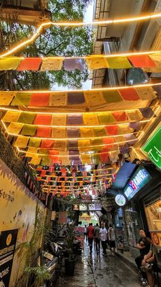 people are walking down an alley way with umbrellas hanging from the ceiling over them