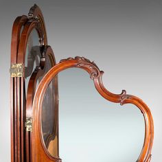 an old fashioned wooden mirror with ornate carvings on it's face and sides, in front of a gray background