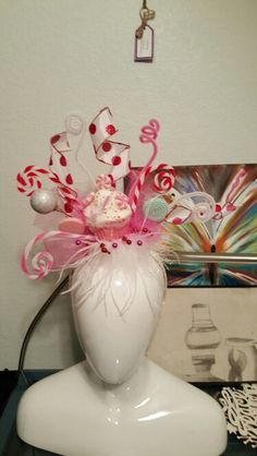 a white vase filled with candy canes on top of a table next to a painting