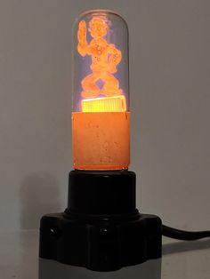 an orange light sitting on top of a black stand next to a white wall and floor