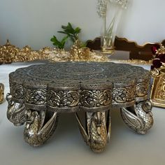 an ornately decorated silver tray on a table with gold decorations and flowers in the background