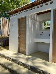 a small white house with wooden doors and steps leading up to the outside bathroom area