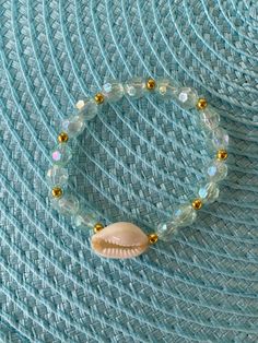 This handmade bracelet has light blue/teal beads with a hint of gold and a seashell charm. This bracelet is perfect for summer time and very fashionable! Cheap Beaded Shell Bracelets, Beach Beads Bracelets, Gold Beaded Bracelets For Beach Season, Beachy Gold Beaded Bracelets, Gold Beaded Beachy Bracelets, Turquoise Beaded Shell Bracelets, Gold Shell Beaded Strand Bracelets, Casual Gold Stretch Bracelet For Beach, Ocean-inspired Gold Beaded Bracelets For Vacation