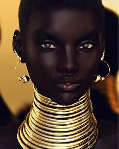 an african woman with gold jewelry on her neck and earrings, looking at the camera